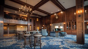 A spacious lobby with a high ceiling, chandeliers, a stone fireplace, and a blue patterned carpet. - The Osthoff Resort (Elkhart Lake)