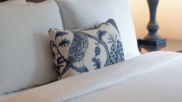 A neatly made bed with white linens and a decorative pillow, a wooden headboard, and a bedside lamp.