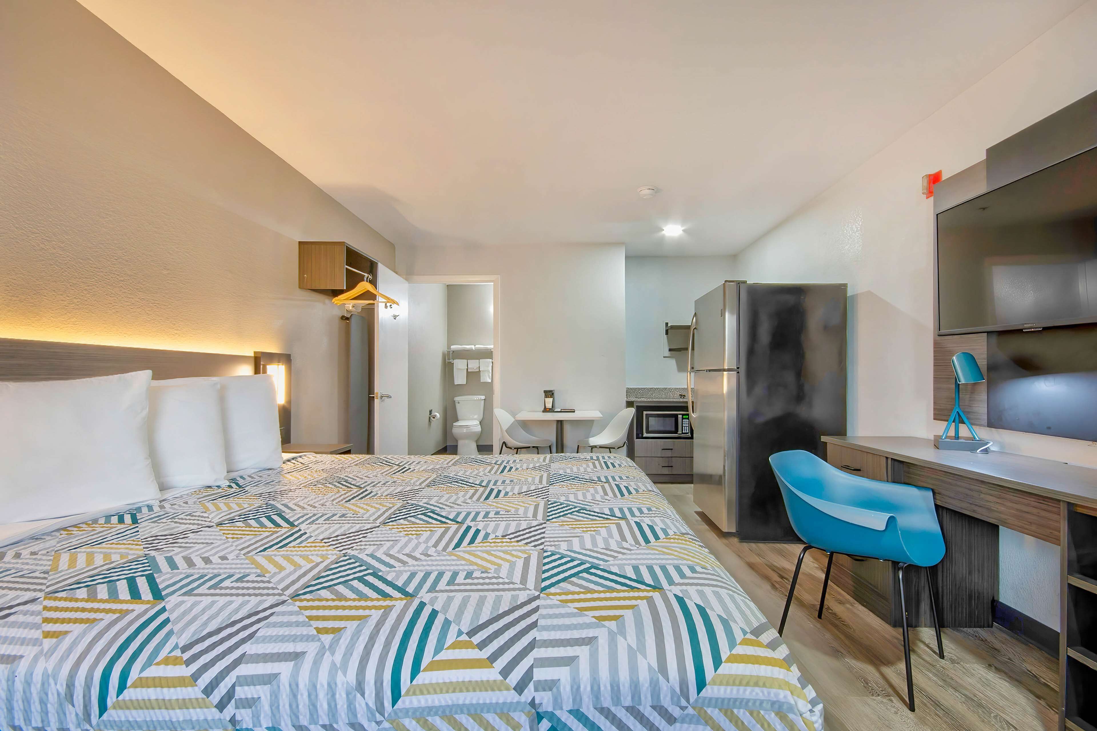 A hotel room with a large bed, a desk with a chair, a microwave, and a TV.