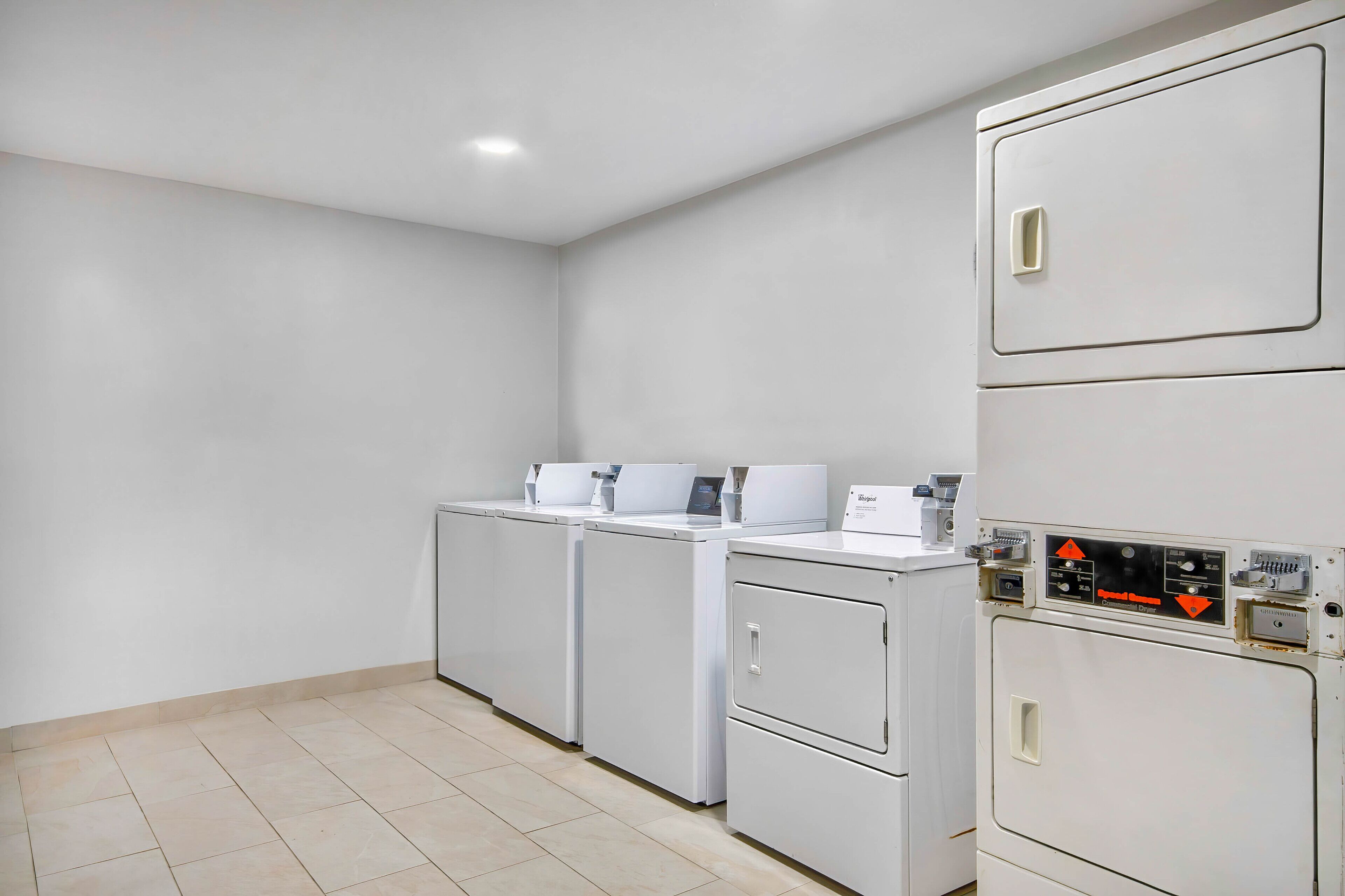 A laundry room with three stacked washers and dryers, a control panel, and a tiled floor.