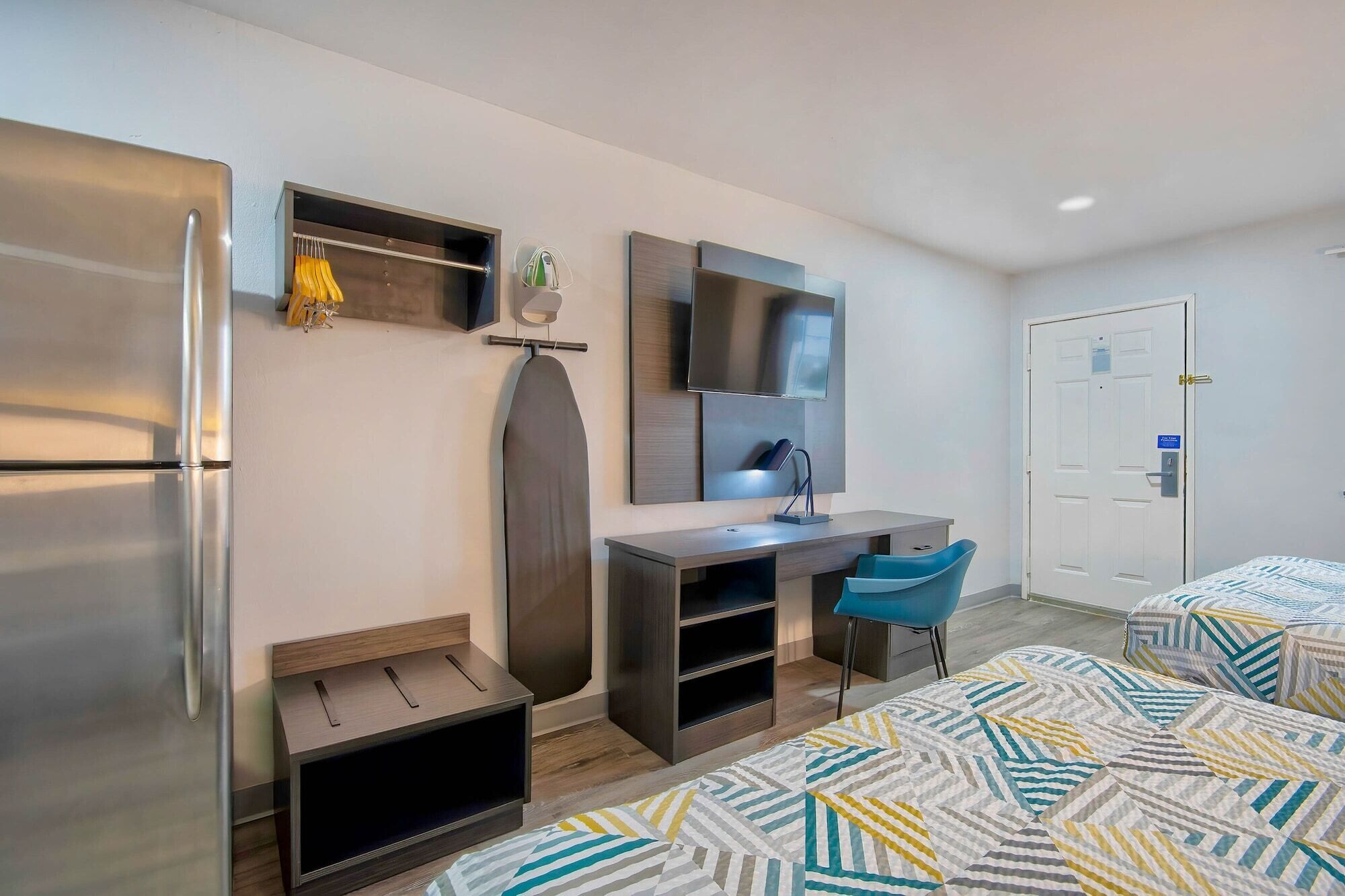 Una habitación de hotel moderna con cama, escritorio, silla, televisor y refrigerador.
