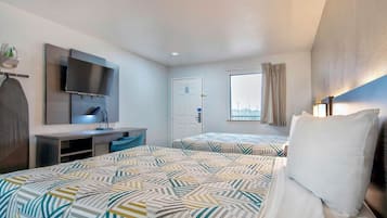 Habitación de hotel con dos camas, un escritorio, un televisor de pantalla plana, una ventana con cortinas y una puerta.