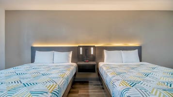 A hotel room with two beds, each with a patterned bedspread, a nightstand with a lamp, and a wall-mounted light fixture.