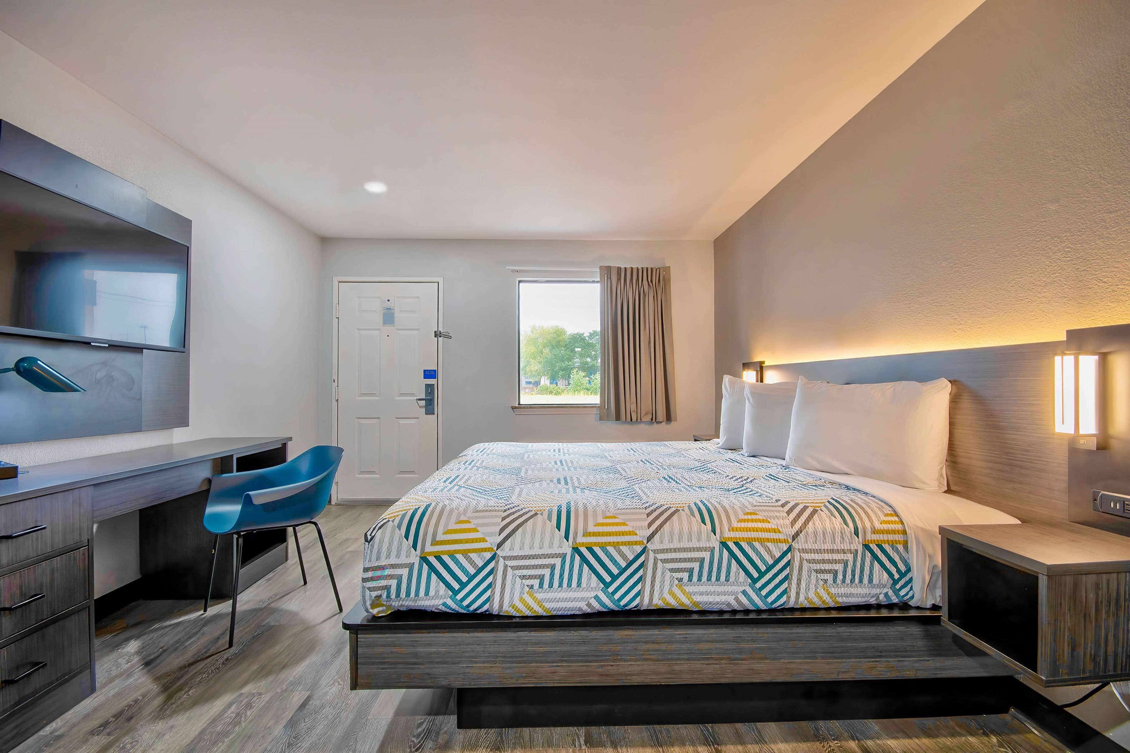 Habitación de hotel moderna con cama, escritorio, silla y un ventanal con cortinas.