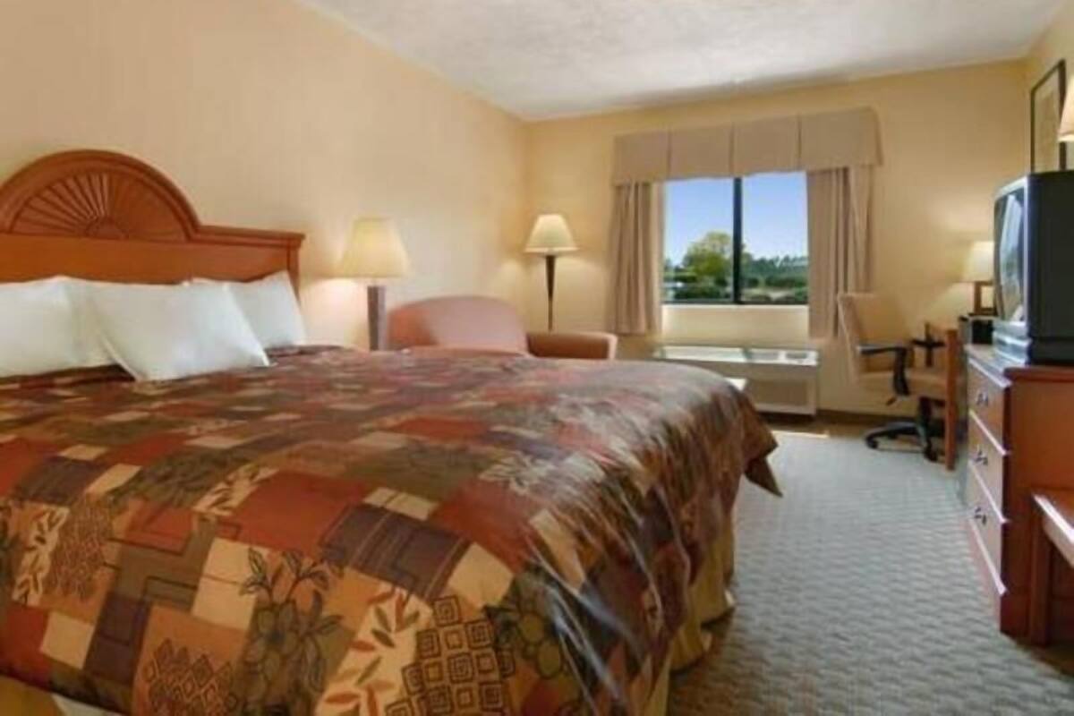 A hotel room with a bed, a desk, a chair, a TV, and a window.