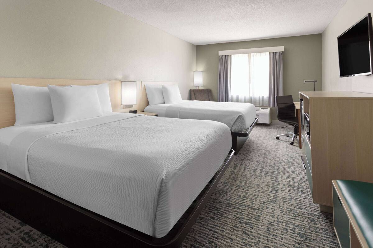 A hotel room with two beds, a desk, a chair, a TV, and a window with curtains.