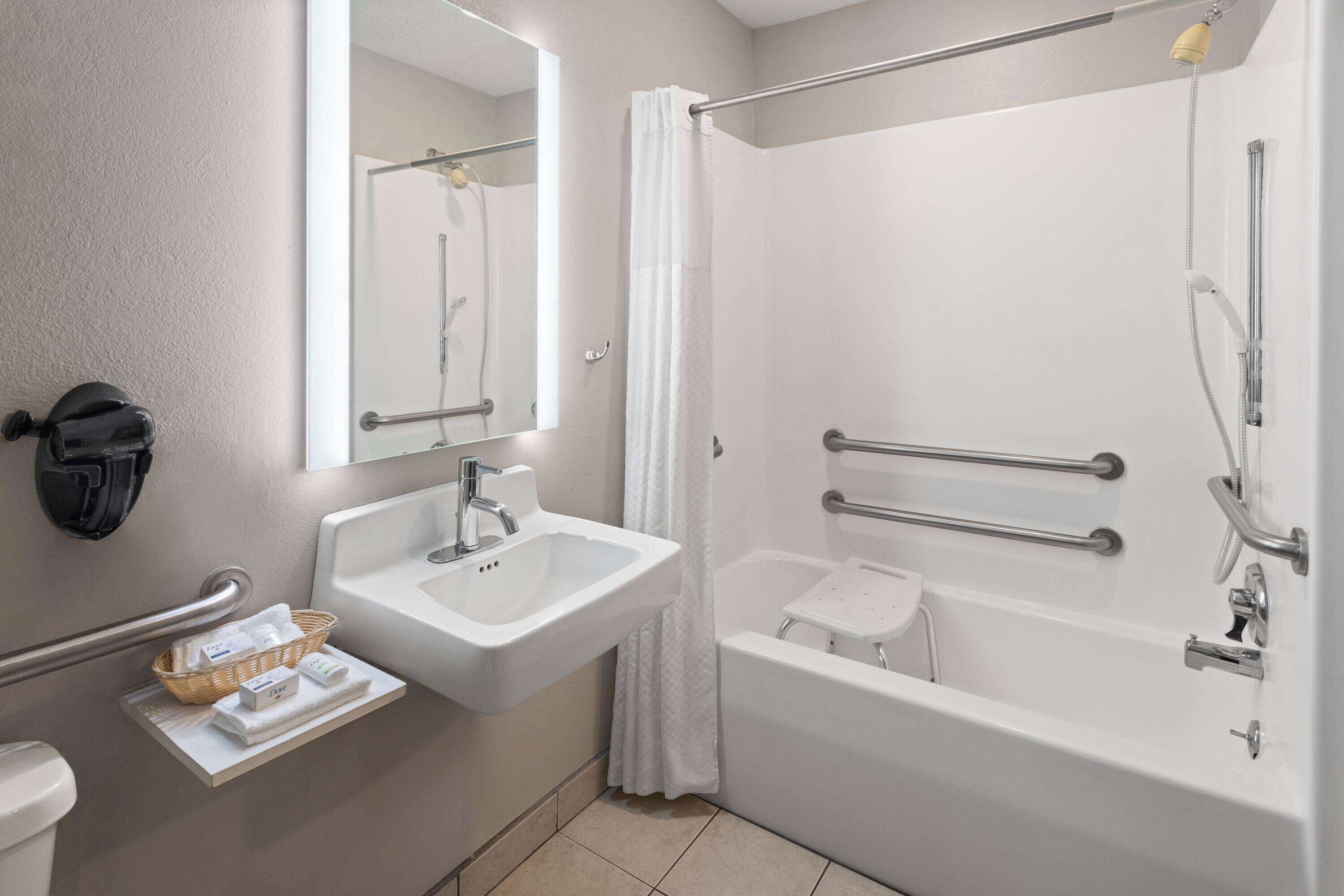 Un baño moderno con lavamanos, espejo, ducha y barras de apoyo.