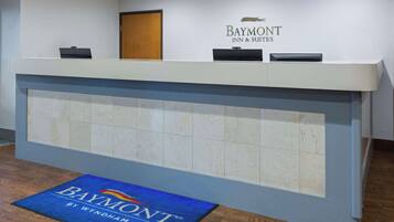Una mesa de recepción con el logotipo de Baymont Inn & Suites, una puerta de madera y un tapete azul con el nombre del hotel.
