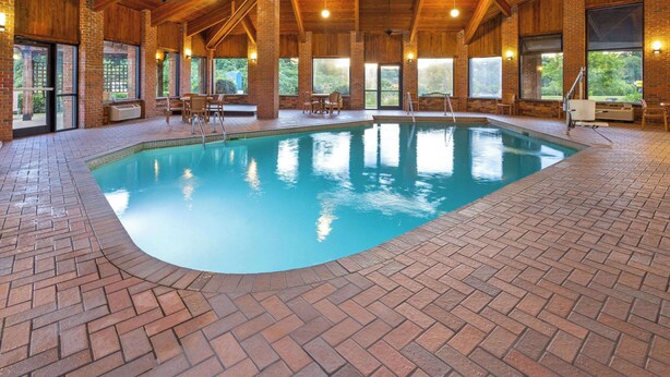 Une piscine intérieure dotée d’un sol en briques, de poutres en bois et de grandes fenêtres.