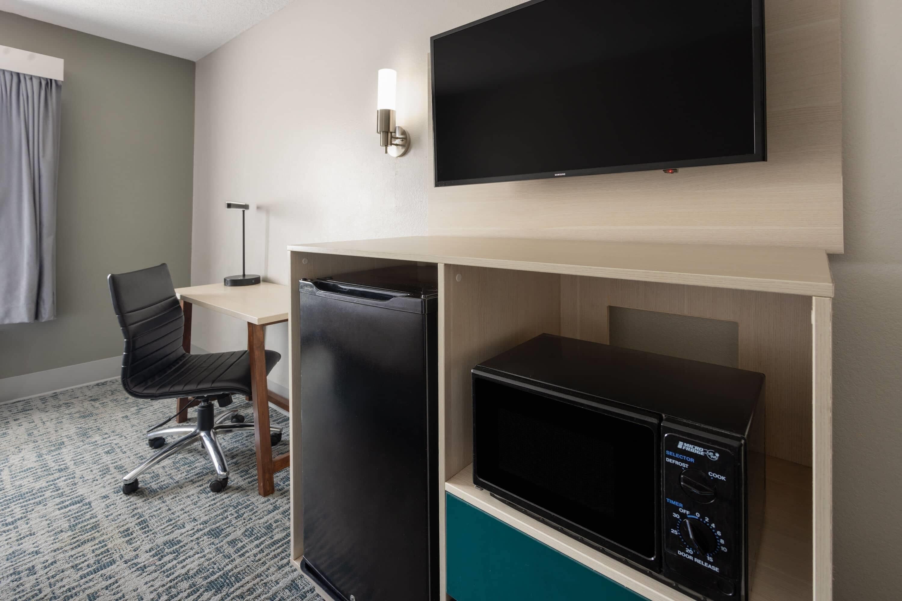Een hotelkamer met een flatscreen televisie, een koelkast, een magnetron, een bureau en een stoel.