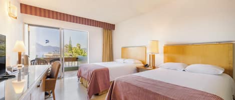 A hotel room with two beds, a desk, a chair, and a balcony with a view.