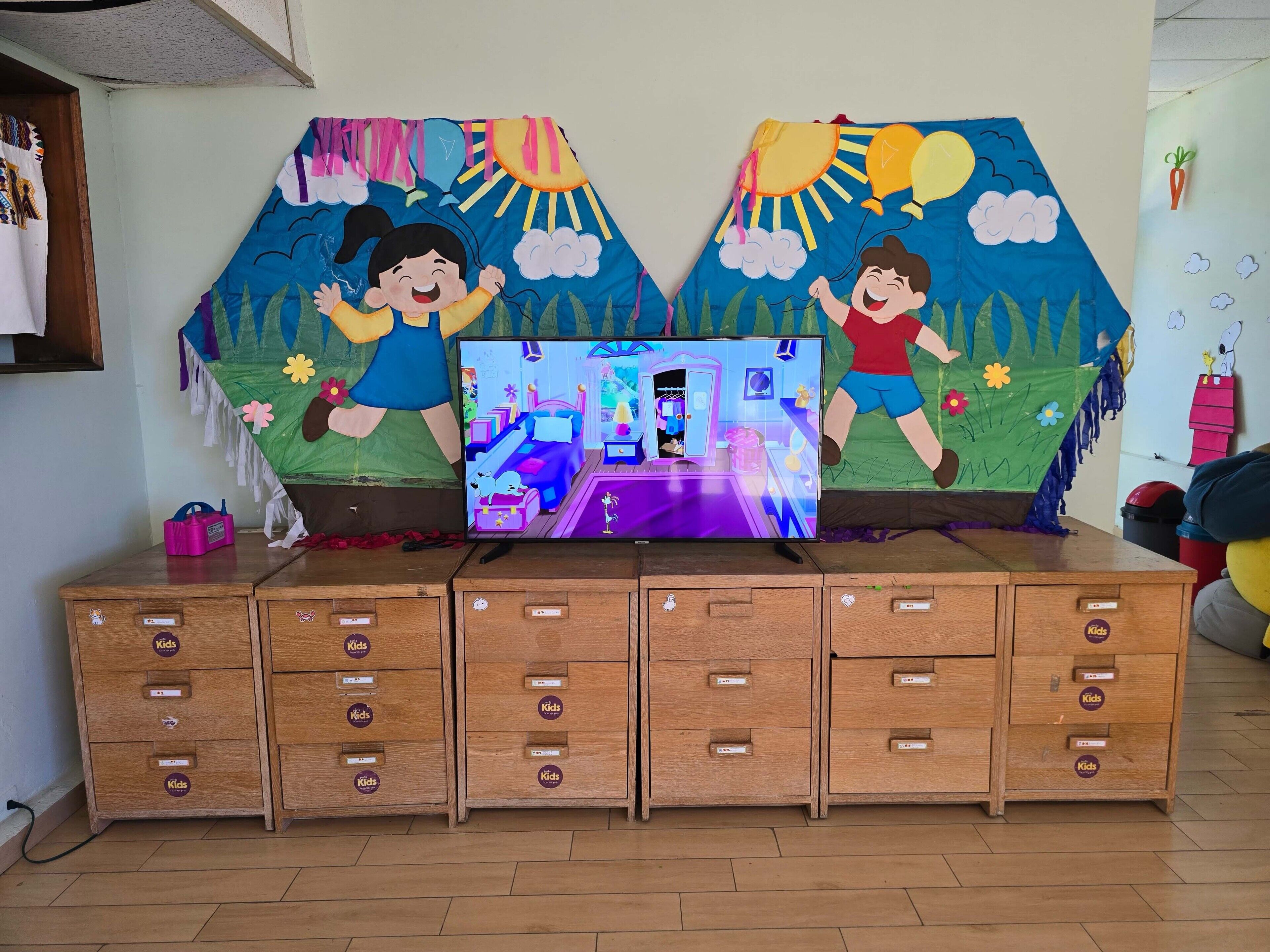 Een speelruimte voor kinderen met een televisie, houten opbergkasten en kleurrijke wanddecoraties.
