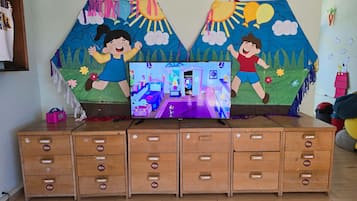 Zona de juegos para niños con televisor, armarios de madera y decoración mural colorida.