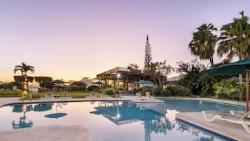 Una piscina con sillas de descanso, una zona de estar techada y palmeras.