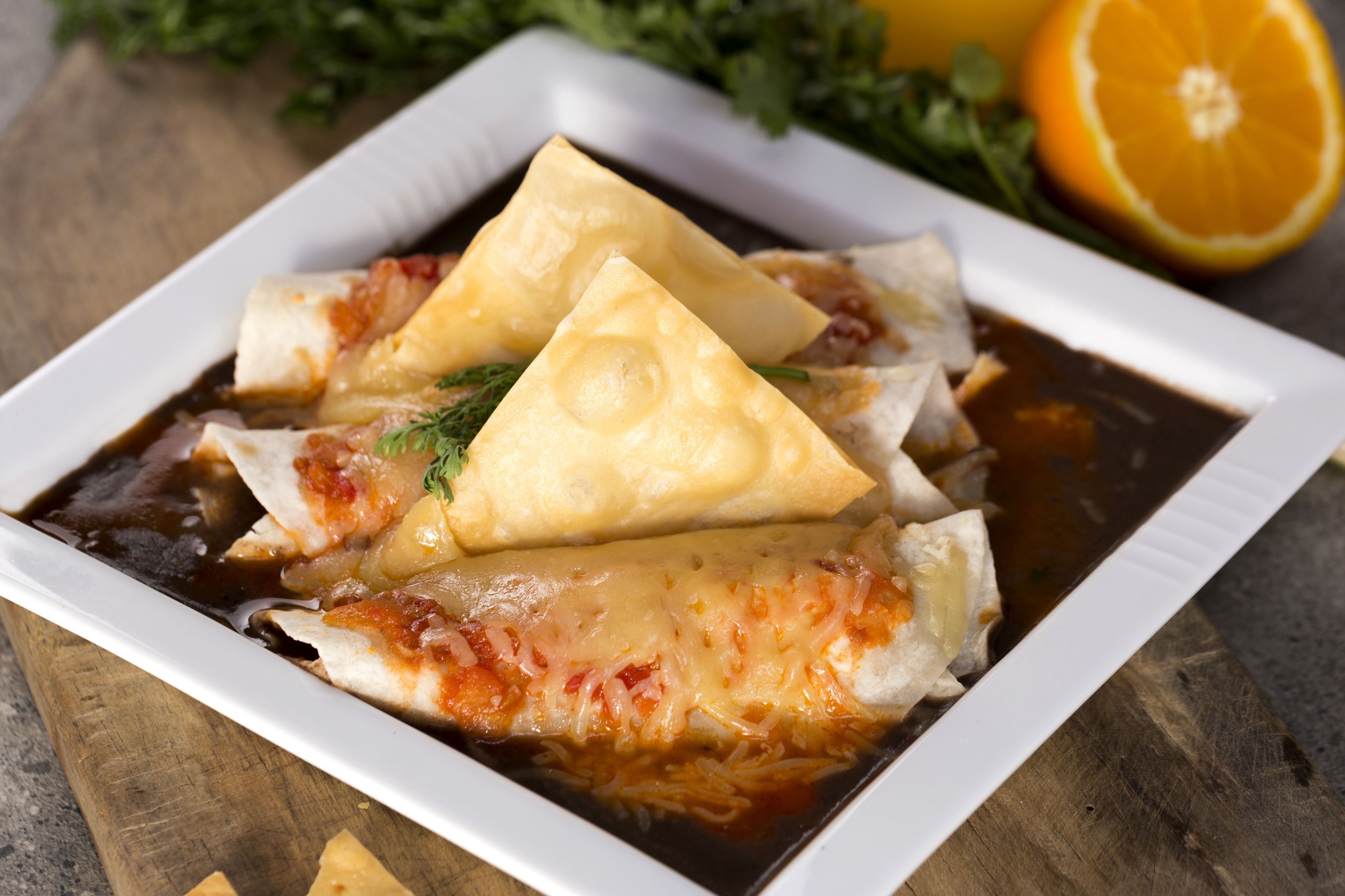 Un plato de enchiladas con queso y salsa, adornado con hierbas, sobre una mesa de madera.
