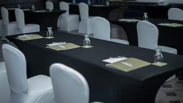 Un salón de conferencias con mesas dispuestas para reuniones, sillas blancas, placas de identificación y vasos de agua.