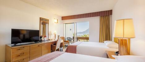 A hotel room with two beds, a desk with a TV, a chair, a lamp, and a view of the outdoors.