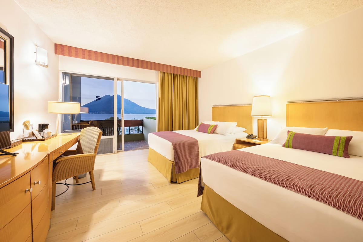 A hotel room with two beds, a desk, a chair, and a view of a mountain.