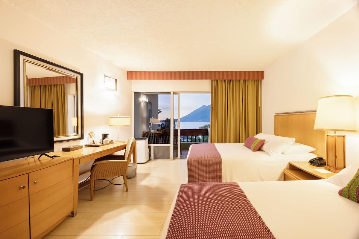 A hotel room with a bed, desk, chair, television, and a view of a mountain.