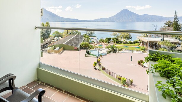 A balcony with a view of a swimming pool, outdoor seating, and a mountainous landscape. - Porta Hotel del Lago (Panajachel)