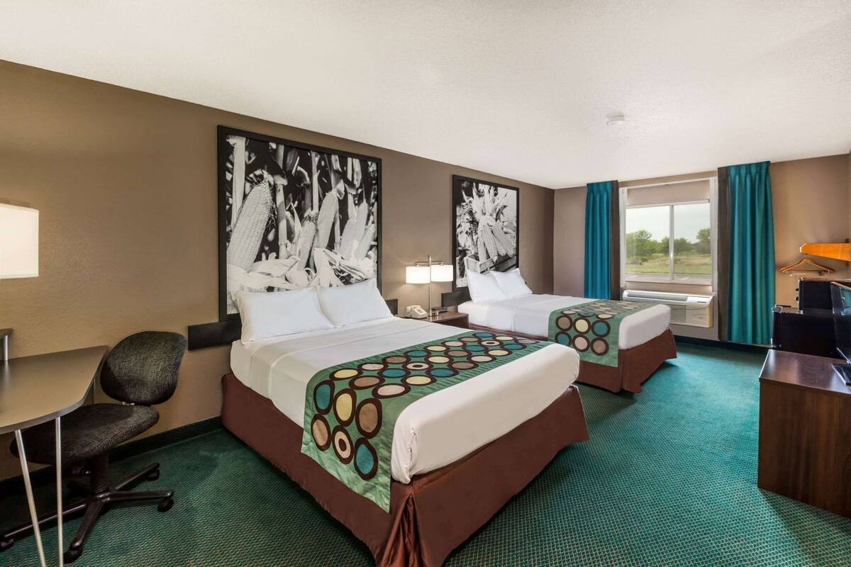 A hotel room with two beds, a desk, a chair, and artwork on the walls.