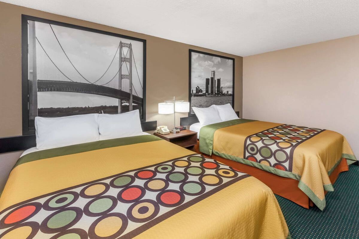A hotel room with two beds, each with a colorful circular-patterned bedspread, a nightstand with a lamp, and framed pictures of a bridge and cityscape on the walls.