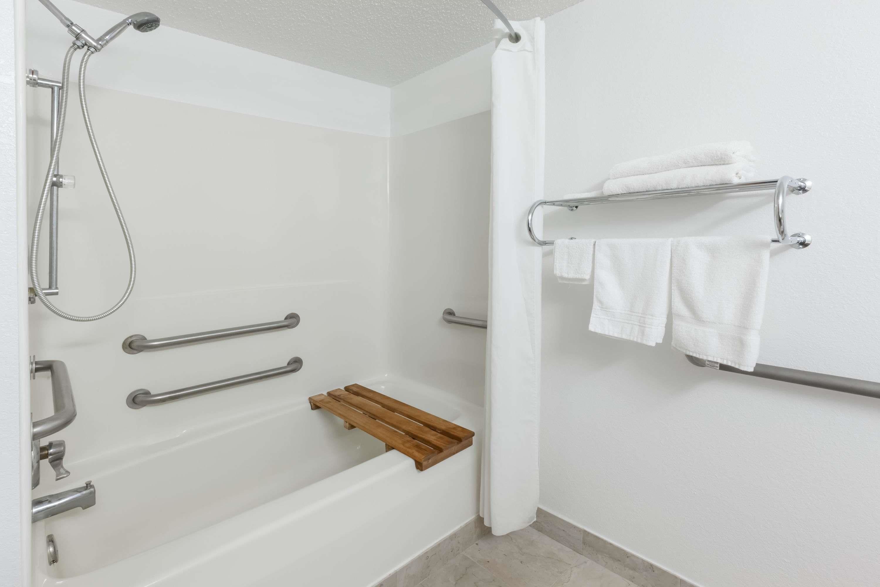 Ein Badezimmer mit Bodendusche, Haltegriffen, einer Holzablage und einem Handtuchhalter.