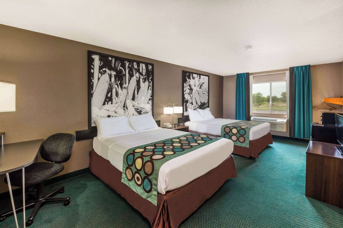 A hotel room with two beds, a desk, a chair, and a desk lamp.
