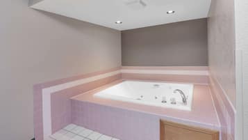 A bathroom with a large bathtub, a wooden cabinet, and a tiled floor.