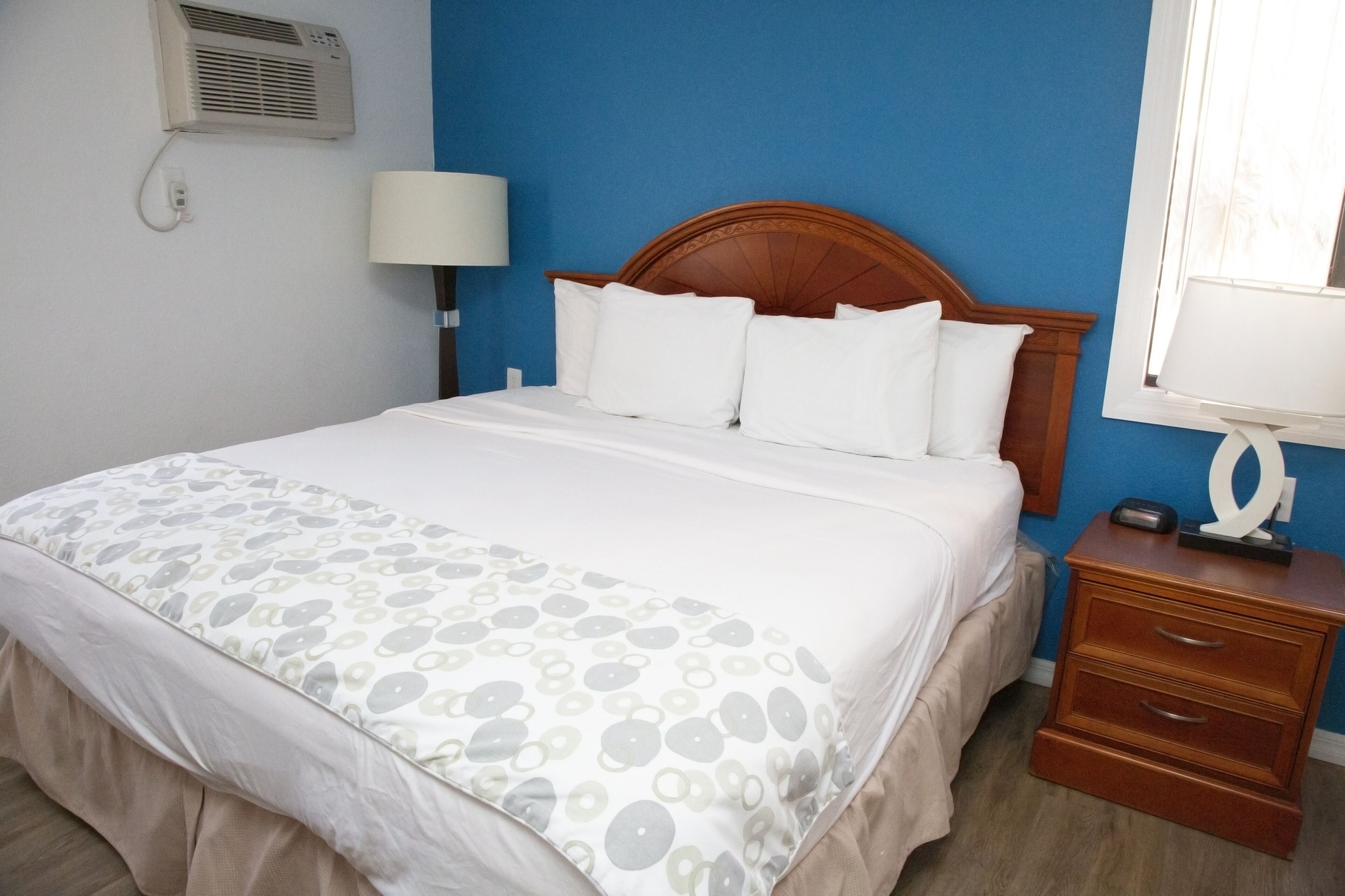 Un letto rifatto con cura, coperto da una trapunta decorata, una testata in legno, una lampada da comodino e un comodino con cassetti.