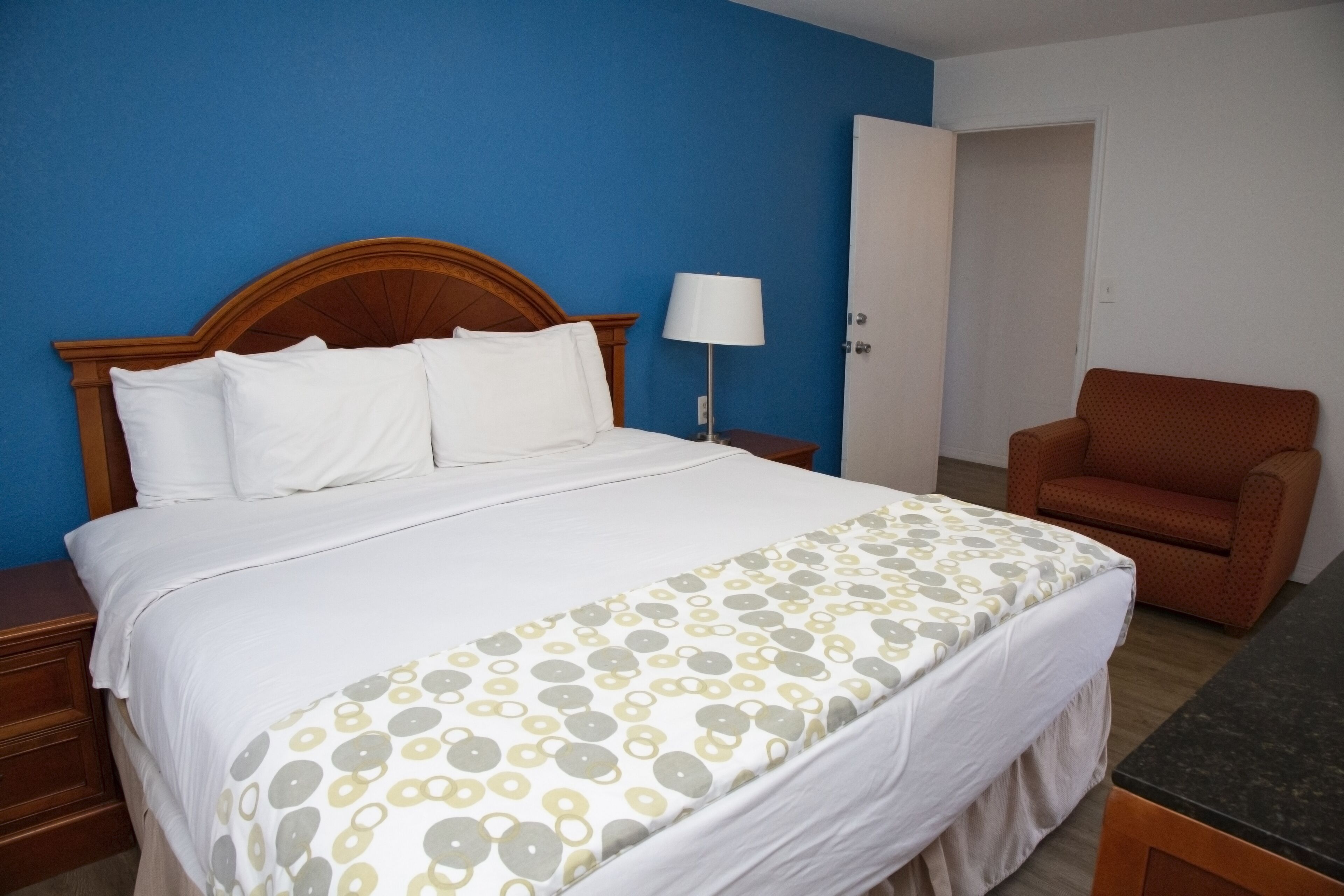 Una habitación de hotel con una cama, una silla, una mesita de noche y una lámpara.