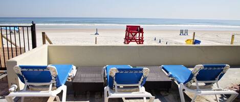 A beachside lounge area with white and blue lounge chairs, a red lifeguard chair, and a yellow bucket.