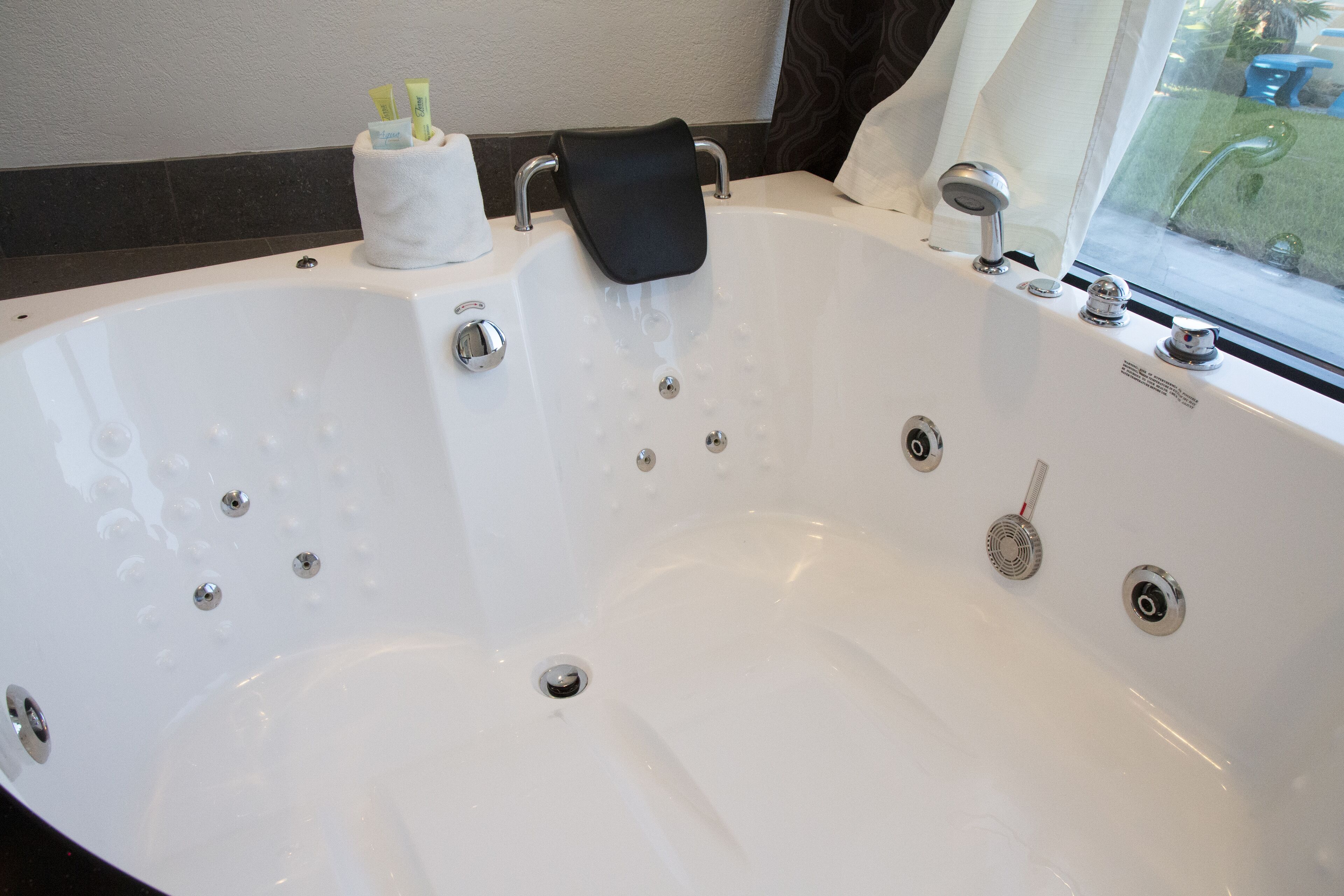 A large white bathtub with multiple faucets and a drain, a towel rack, and a cup holder with toiletries.