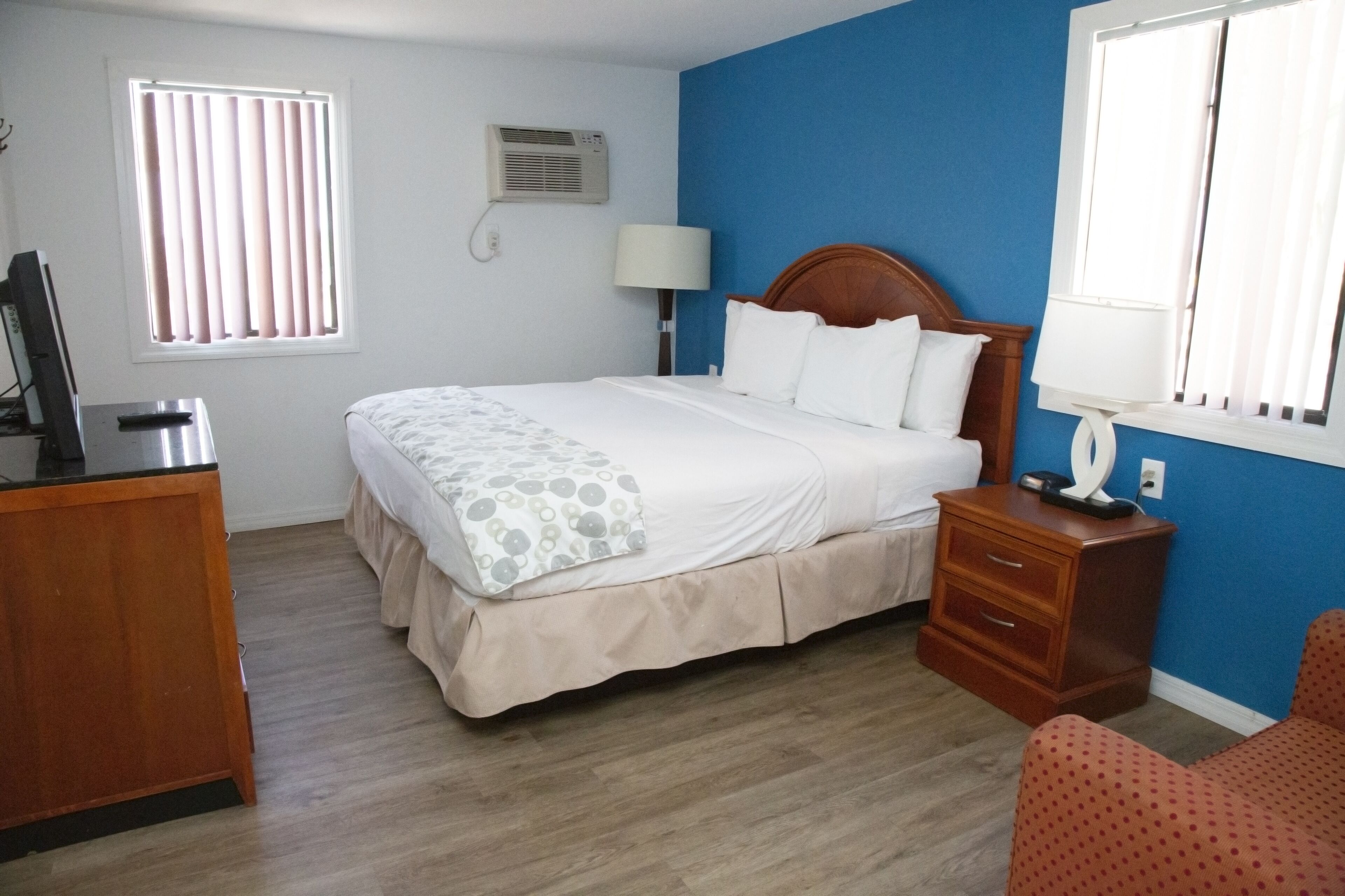 A bedroom with a bed, bedside table, lamp, and a dresser.