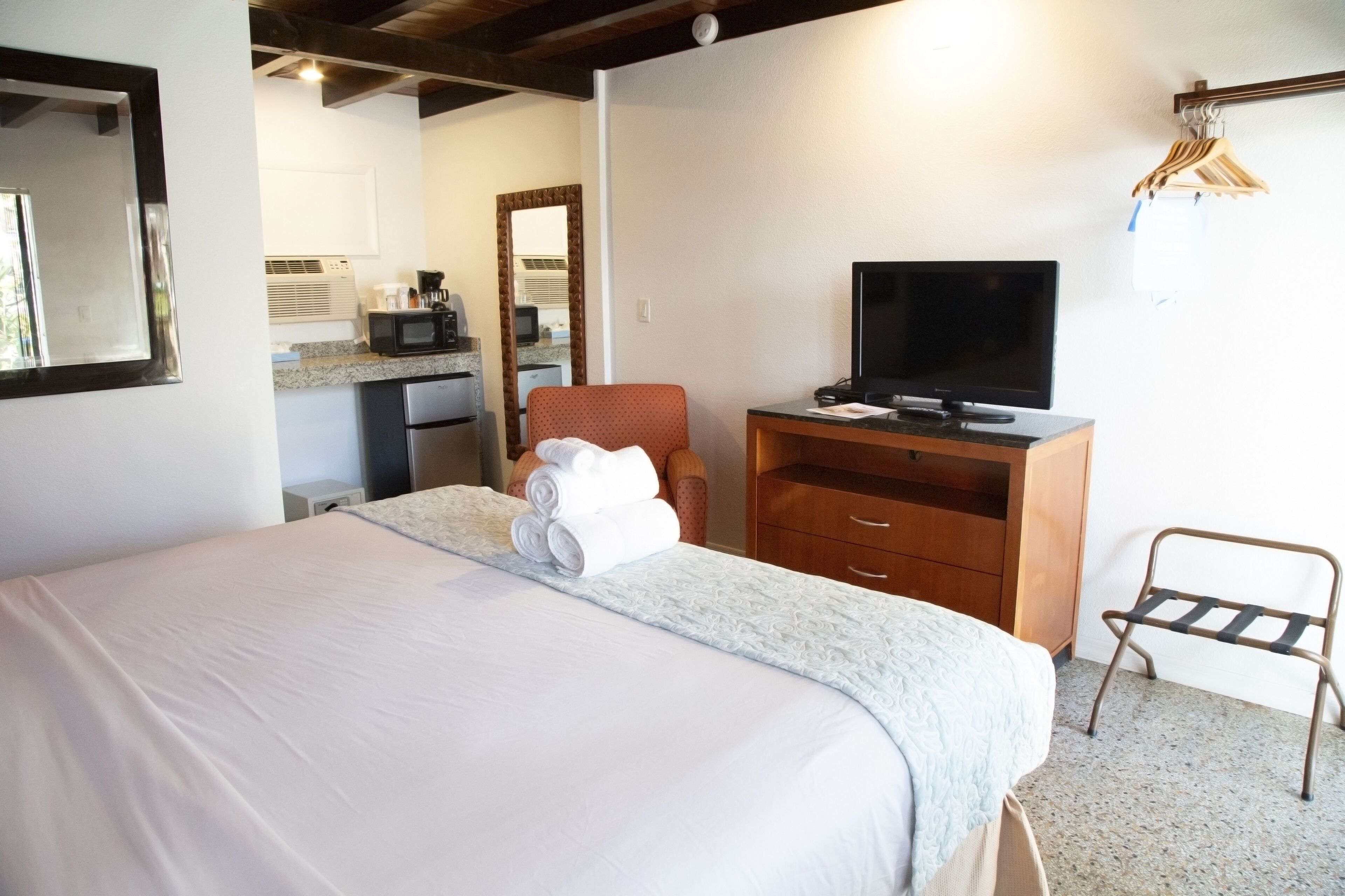 A hotel room with a bed, a TV, a wooden dresser, and a small desk.