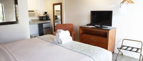 A hotel room with a bed, a TV, a wooden dresser, and a small desk.