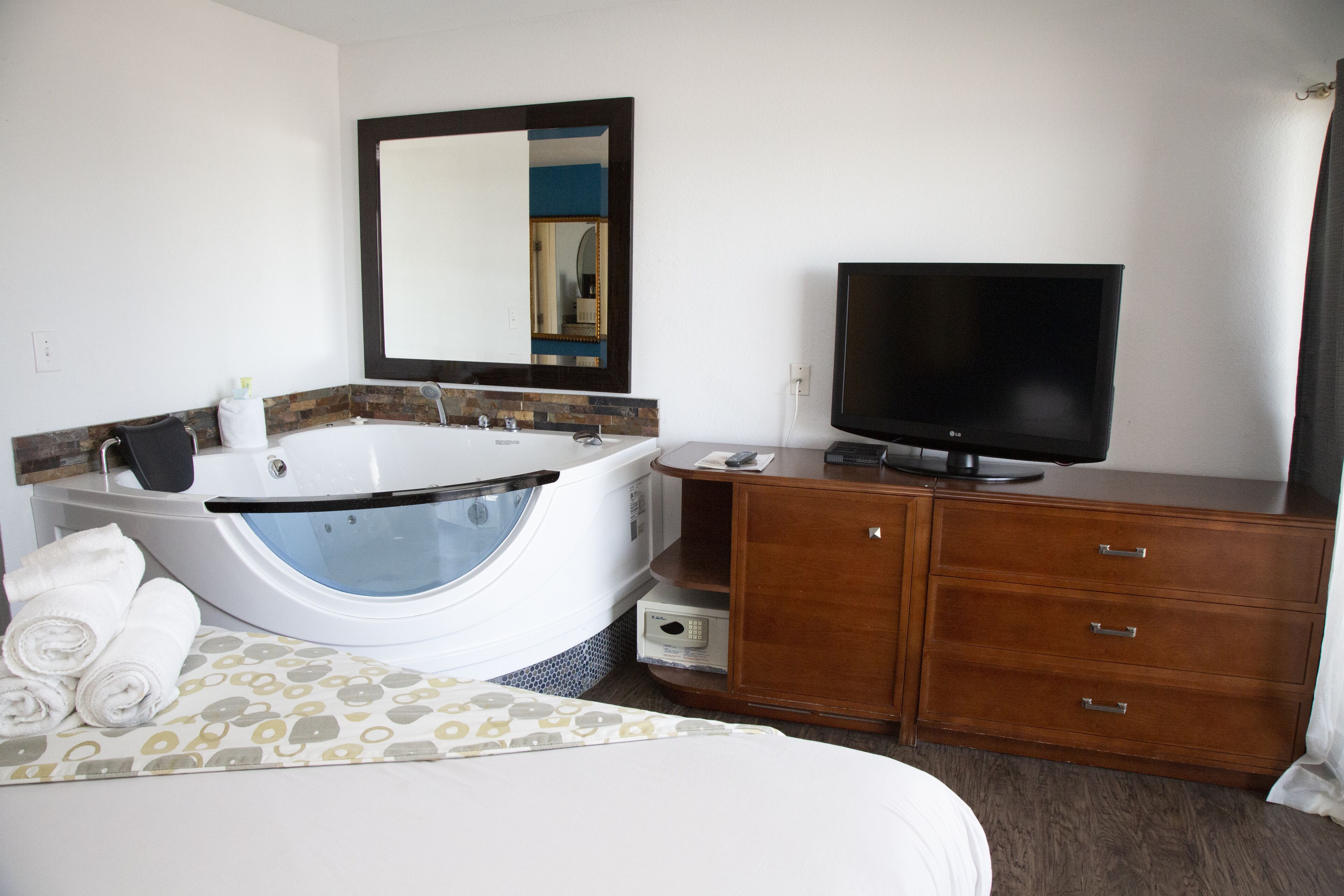 A hotel room with a large bathtub, a wooden cabinet, a flat-screen TV, and neatly folded towels on the bed.