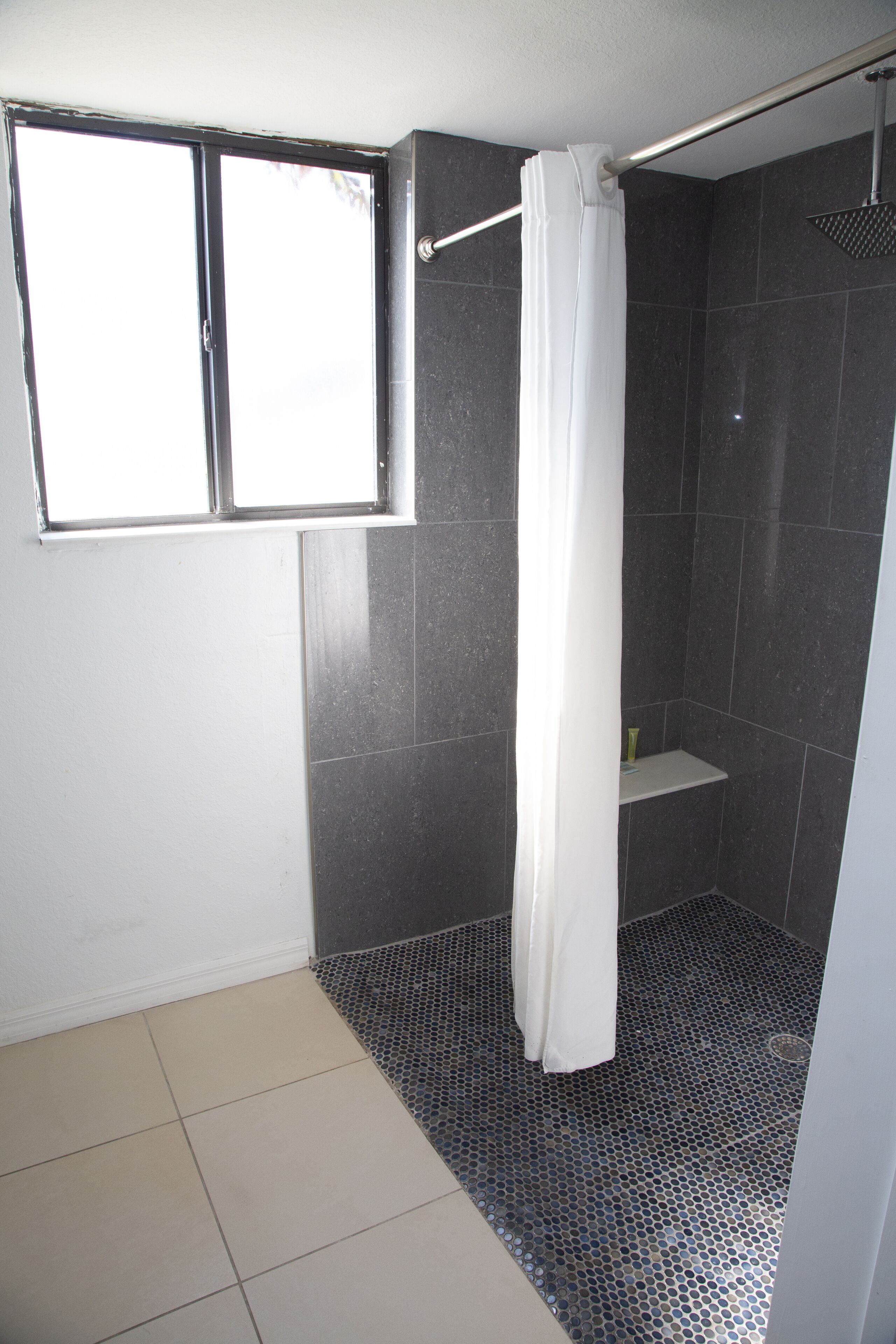 A bathroom with a shower, a window, and a tiled floor.