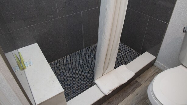 Ein Badezimmer mit dunkel gefliesten Wänden, einer Dusche mit weißer Duschvorhang, einem weißen Waschbecken und einer Toilette.