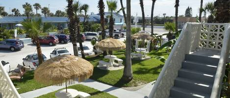 A hotel parking lot with several cars, a staircase, and thatched umbrellas.
