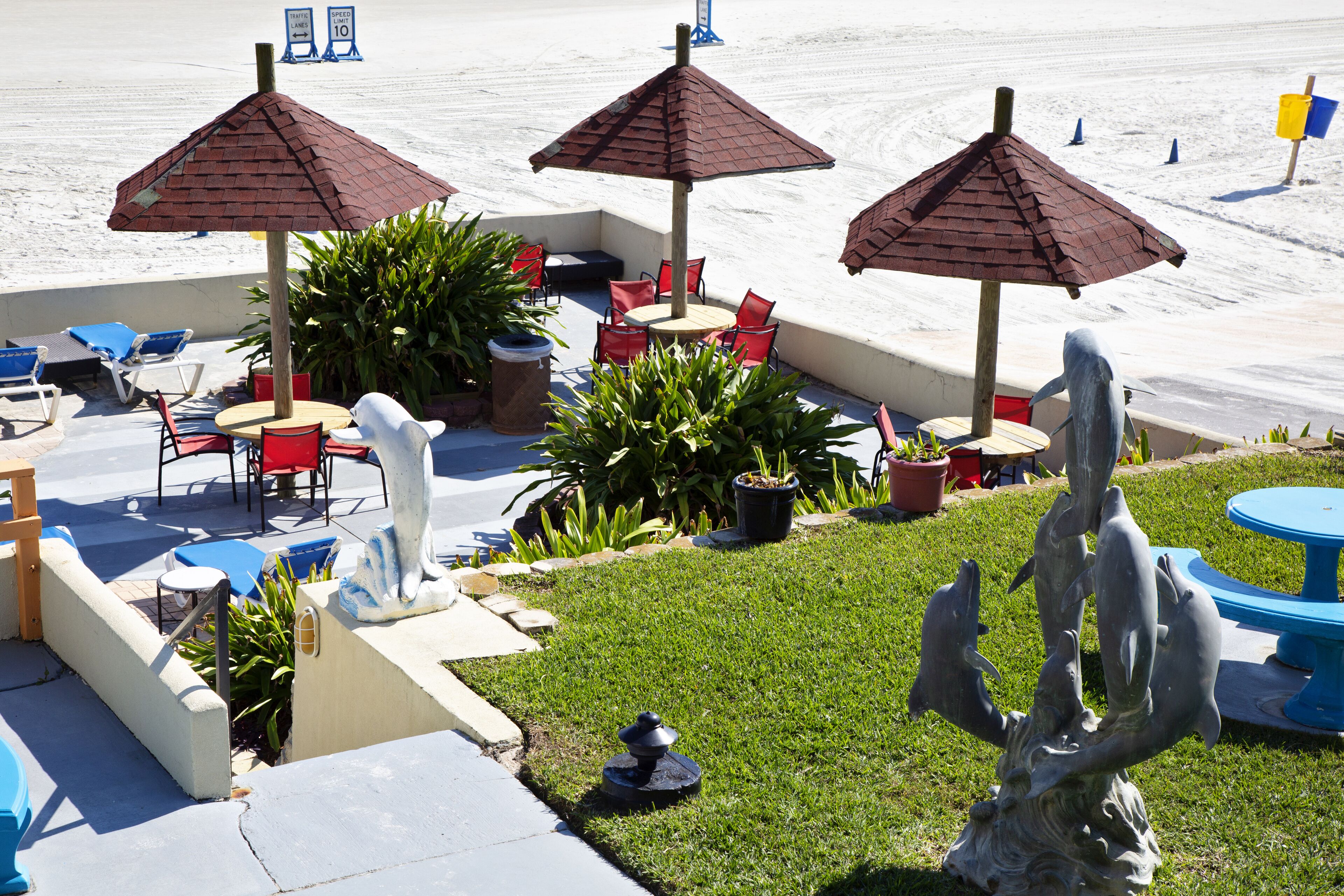 Un espace extérieur aménagé en terrasse, avec des chaises rouges, des tables bleues et des parasols marron.