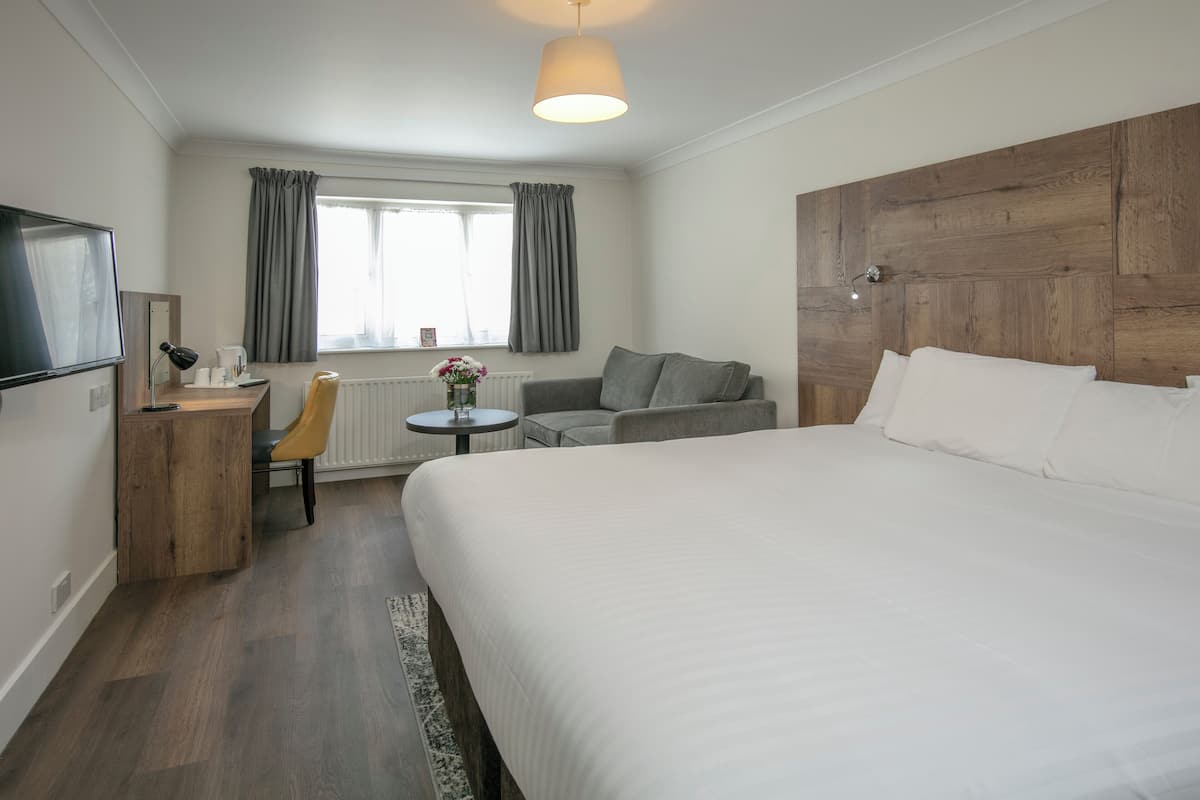 Een hotelkamer met een groot bed, een bureau met stoel, een kleine tafel met lamp, een bank en een televisie aan de muur.