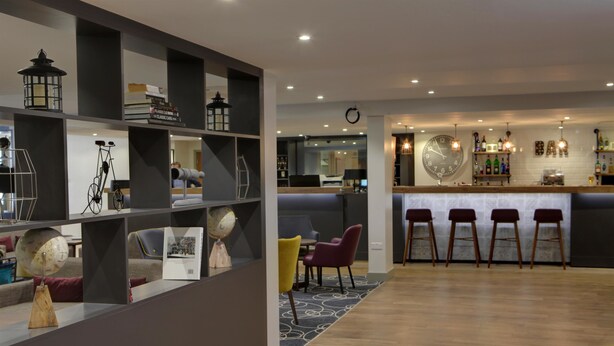 Un intérieur moderne avec un espace bar, un plancher en bois et un coin salon composé de chaises et d’un canapé.