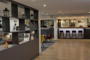 Un interior moderno con una zona de bar, suelo de madera y una distribución de asientos con sillas y un sofá.