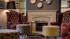 Une pièce avec des fauteuils en cuir, un pouf à motifs, une petite table et une cheminée.