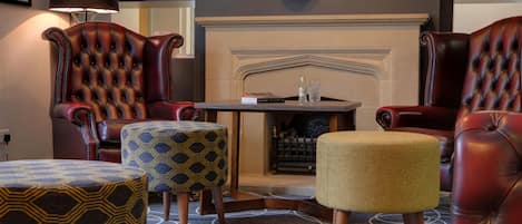 A room with leather armchairs, a patterned ottoman, a small table, and a fireplace.