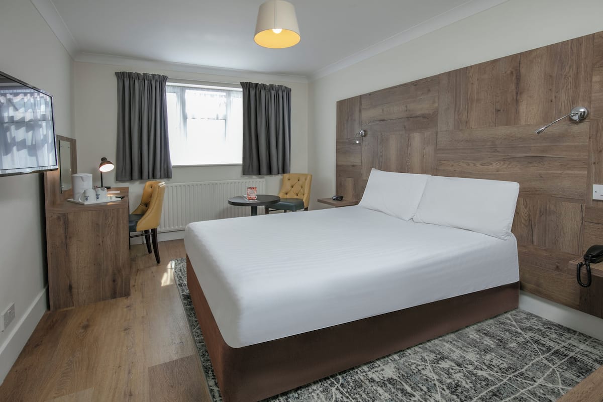 Een hotelkamer met een groot bed, een bureau met stoel, een kleine tafel en een televisie aan de muur.