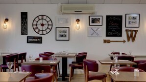 Un restaurant avec des tables et des chaises, des tableaux encadrés au mur et une horloge.