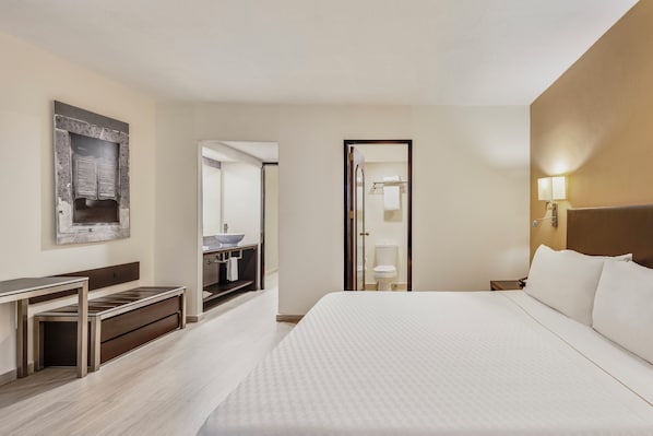 A hotel room with a bed, a desk, a mirror, and a bathroom visible through an open door.