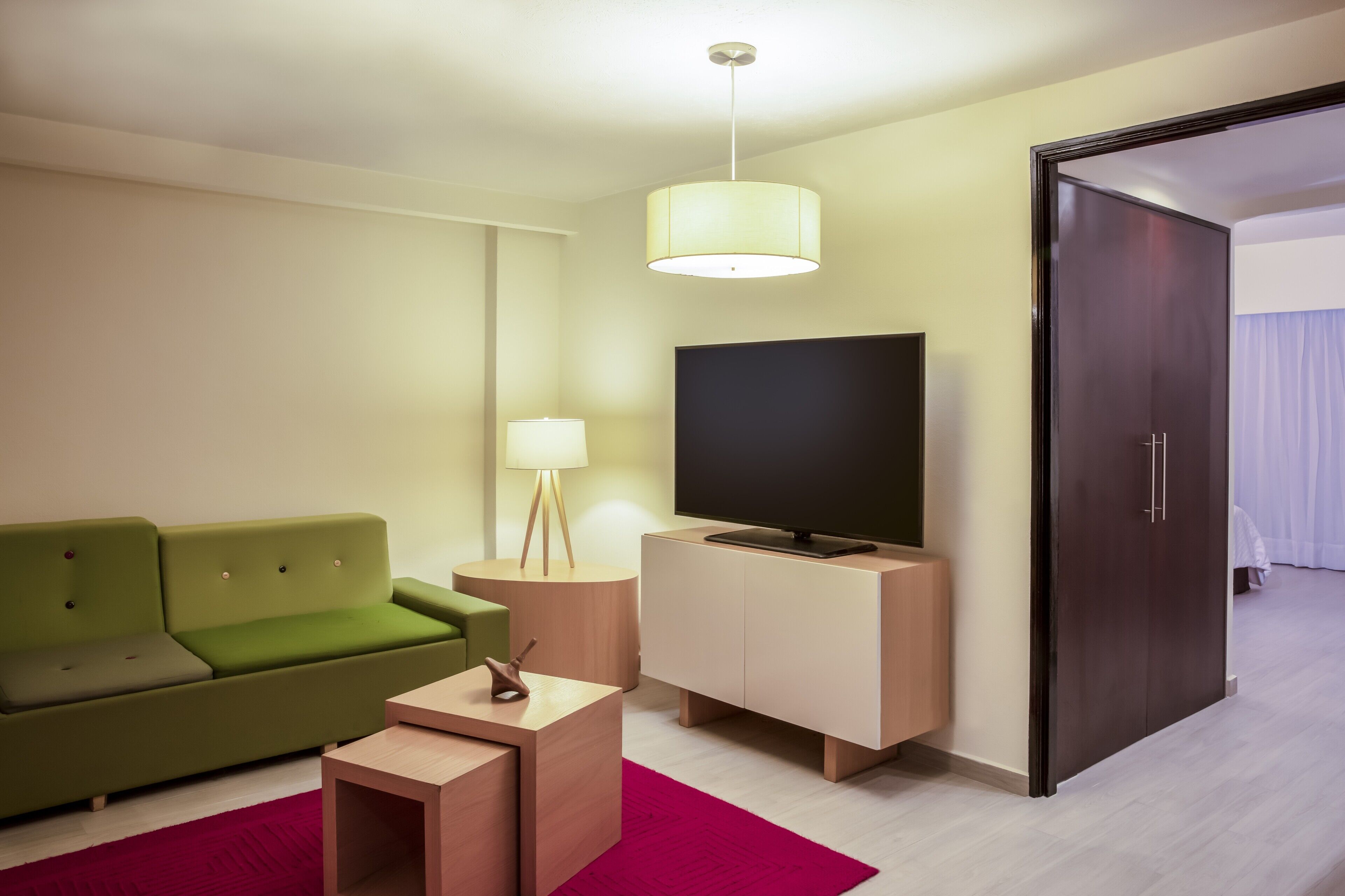 A modern hotel room with a green sofa, a flat-screen TV, a wooden side table, and a dark wardrobe.